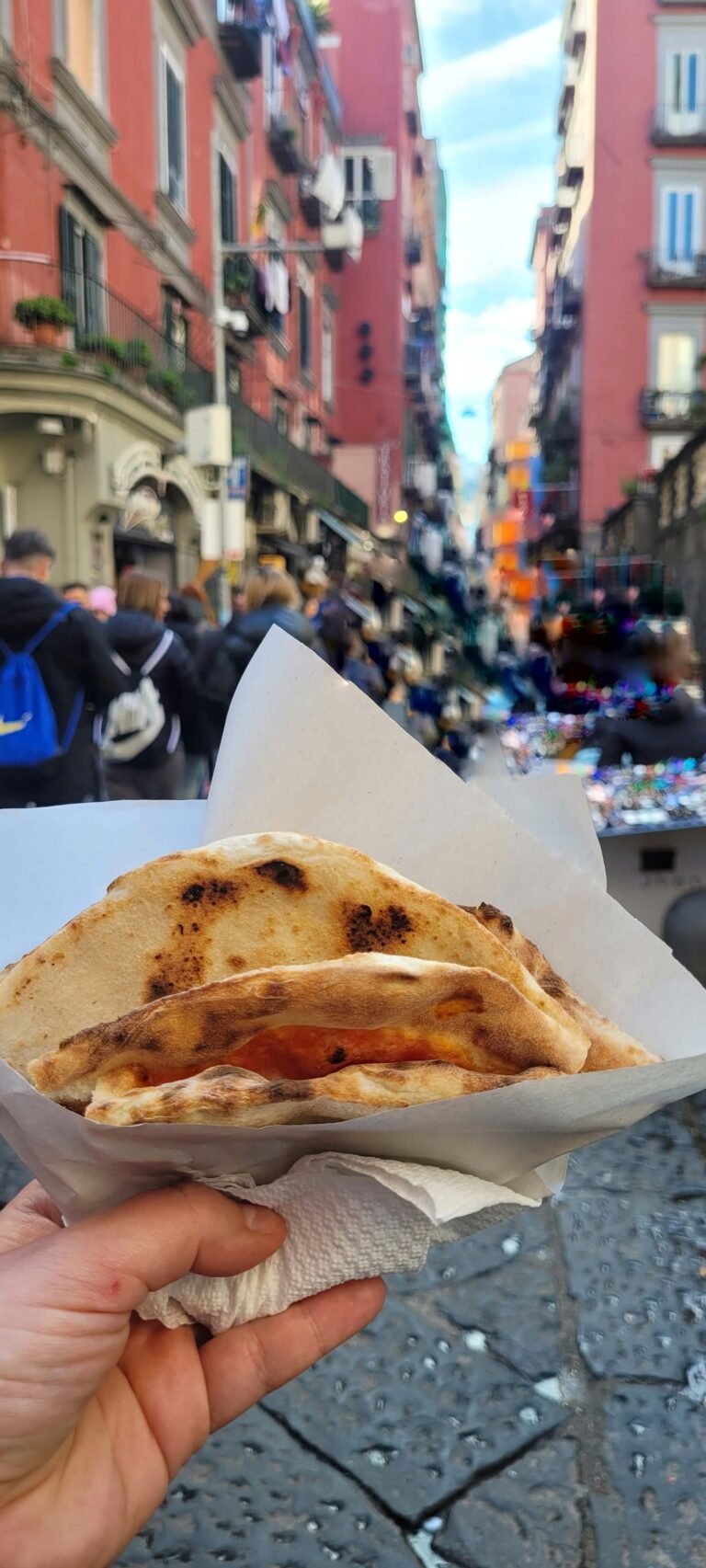 Na zdjęciu widoczna jest pizza a portafoglio - neapolitański przysmak. W tle znajduje się nieostra główna ulica Centro Storico.